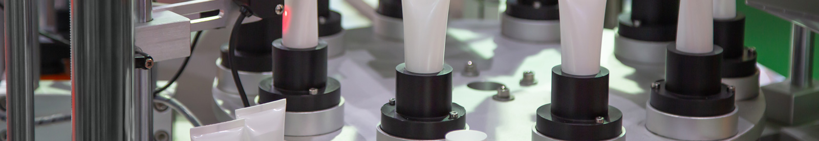 Close up of white body lotion tubes in factory machine